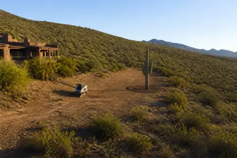 Stucco home at the desert edge with a freshly thinned defensible space band, one saguaro preserved with a clearance radius inside the cleared zone